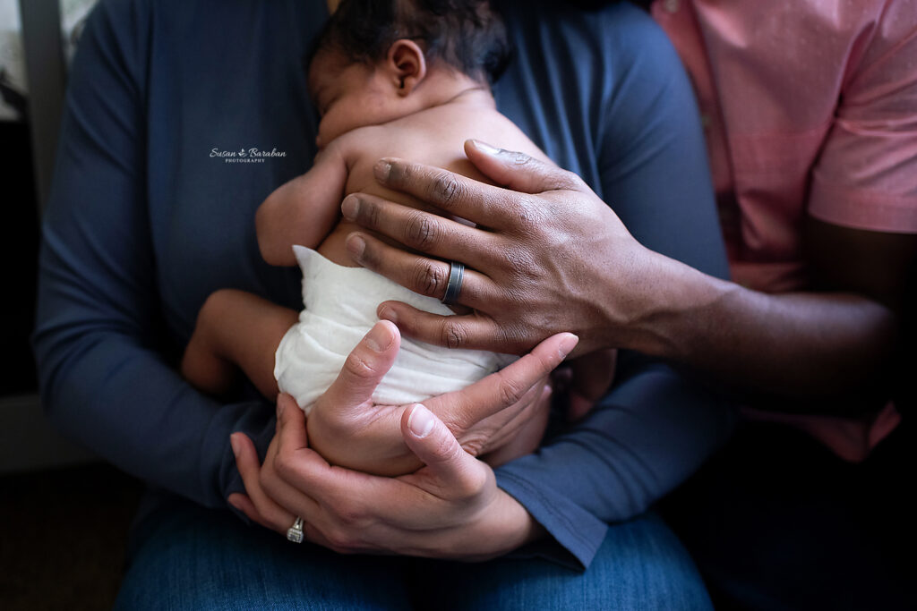 Detail image of parent's hands holding their sleeping newborn son at his newborn photo shoot with Dallas newborn photographer Susan Baraban Photography.