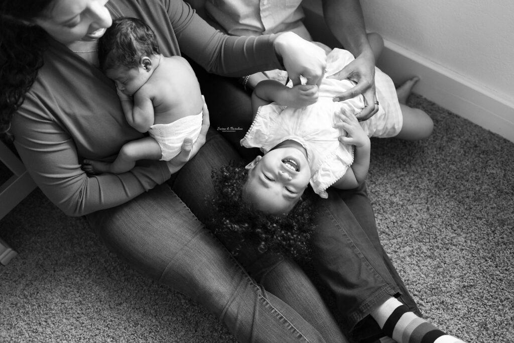 Black and white image of a family of four having fun playing during a lifestyle newborn photo shoot in Dallas, TX.