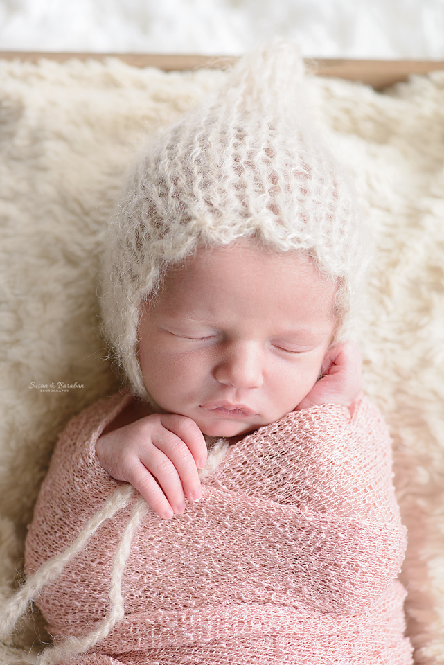 Portrait of a sleeping newborn baby girl wearing a pink swaddle and a mohair bonnet during her newborn photo shoot with Susan Baraban Photography.