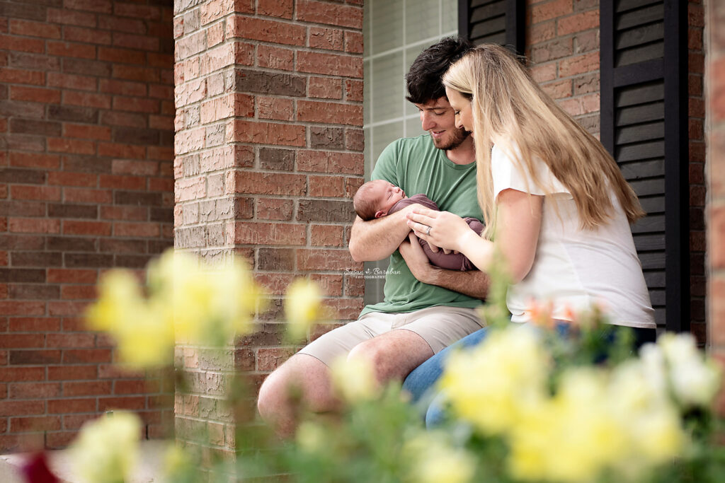 Parents holding their newborn baby while sitting on their front porch in Allen, TX