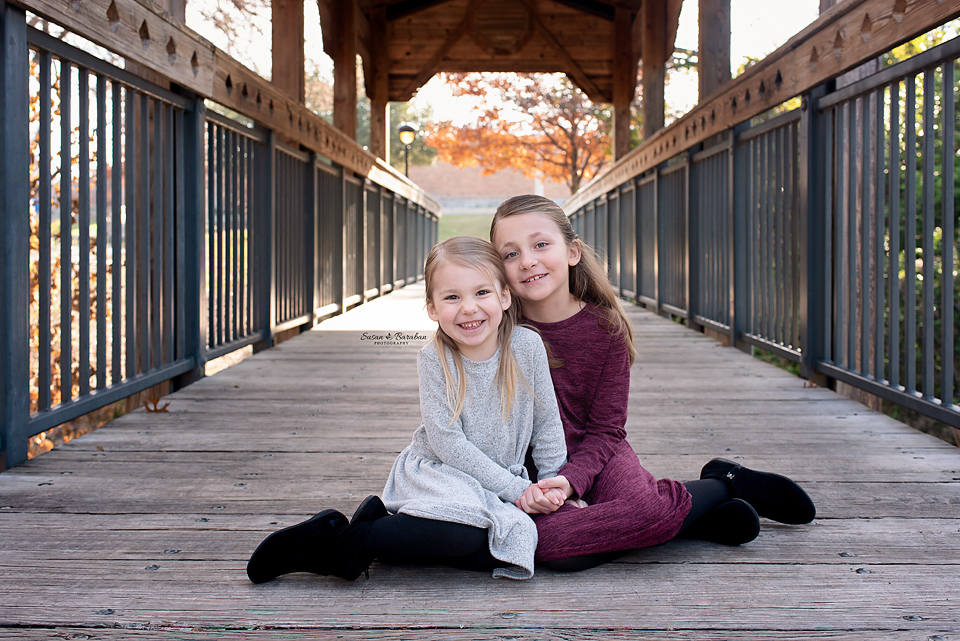 Sisters sitting on a bridge holding hands during their lifestyle family photo shoot.