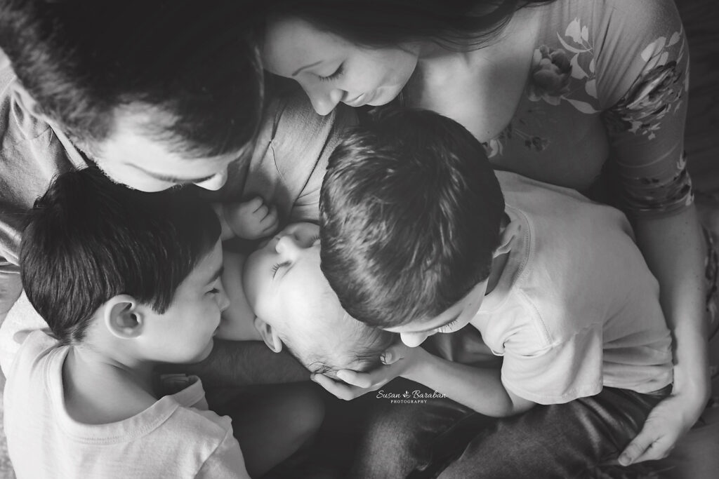 Black & white image of a family huddling together and cuddling a newborn baby girl.