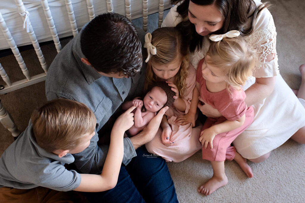 Lifestyle Newborn photographer captured an image of a family of 6 sitting on the floor of a newborn nursery cuddling a newborn baby boy in Prosper, TX.