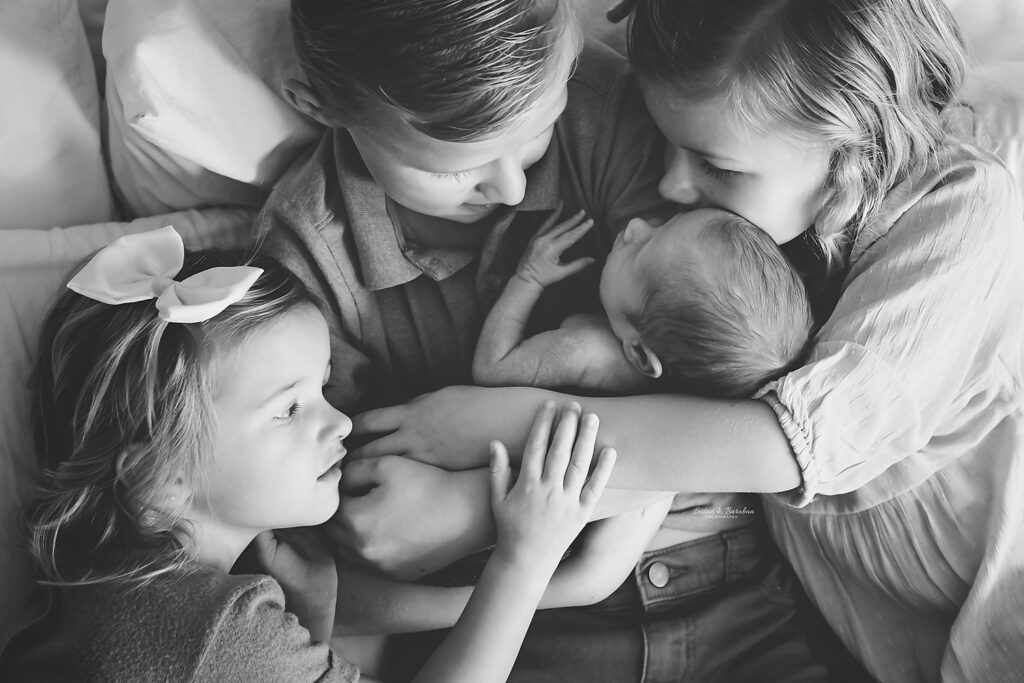 Prosper newborn photographer captured this black and white image of 3 older siblings cuddling their brand new baby brother at his lifestyle newborn session.
