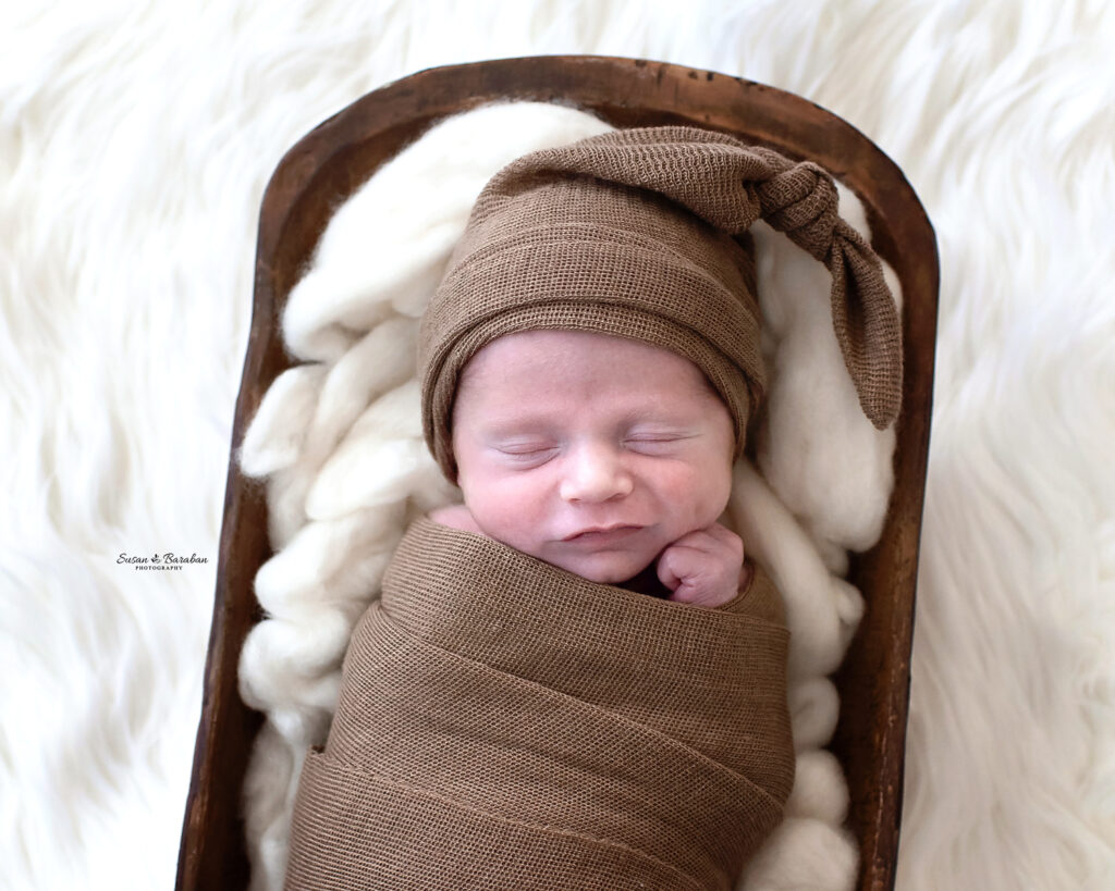 Newborn boy with dimples in a matching swaddle and knot hat at his lifestyle newborn photo session in Richardson, TX.