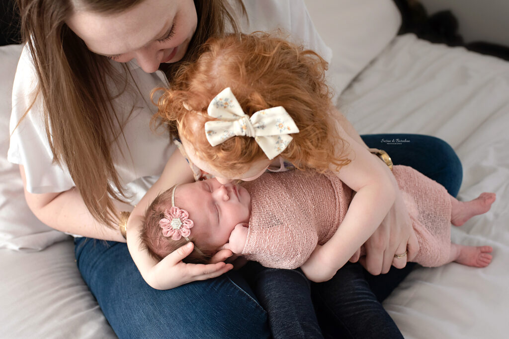 Richardson newborn photographer capturing big sister kissing her newborn baby sister.