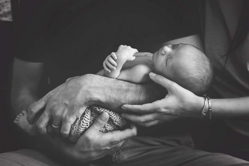 Black and white image of a newborn baby boy sleeping peacefully in his parent's arms.